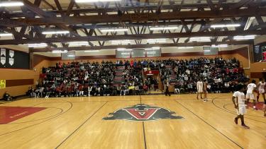 School gym filled with students and staff for a basketball game.